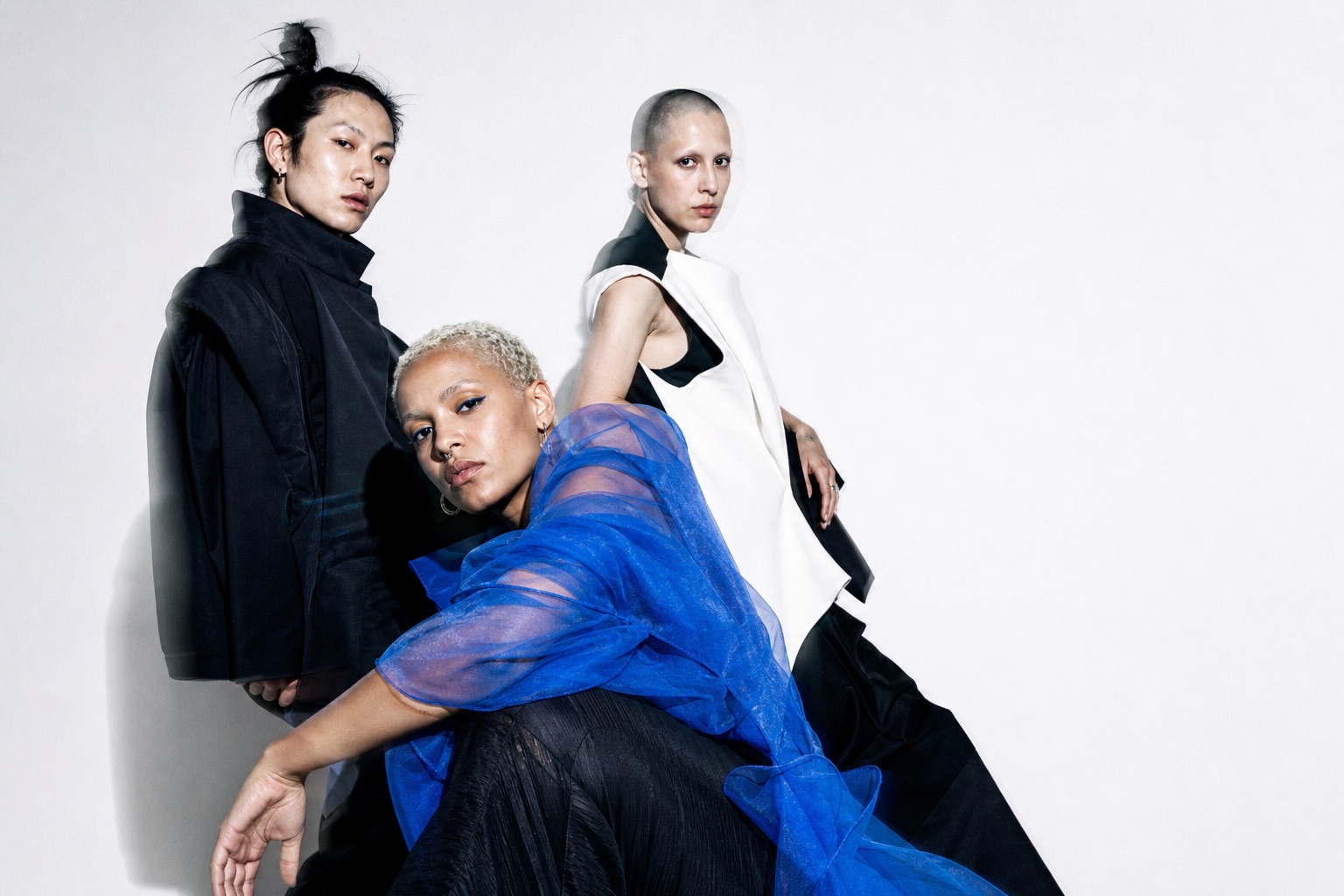 Three experimental performers in sculptural black, white, and blue clothing