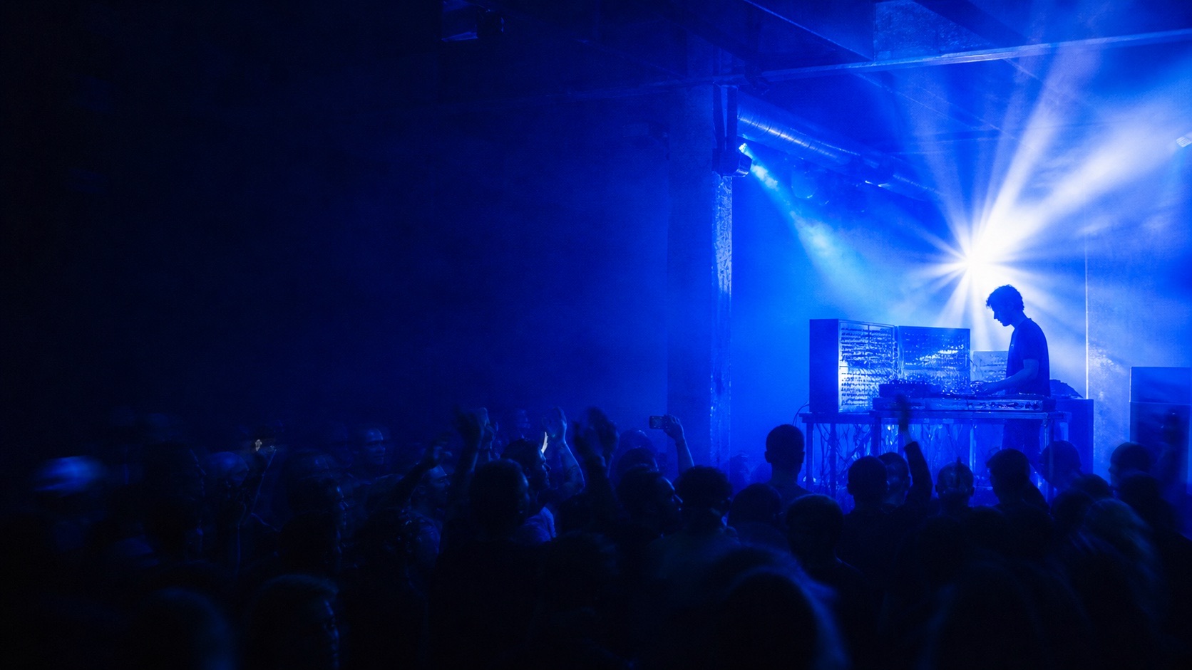 Electronic artist performing in blue light before a crowd